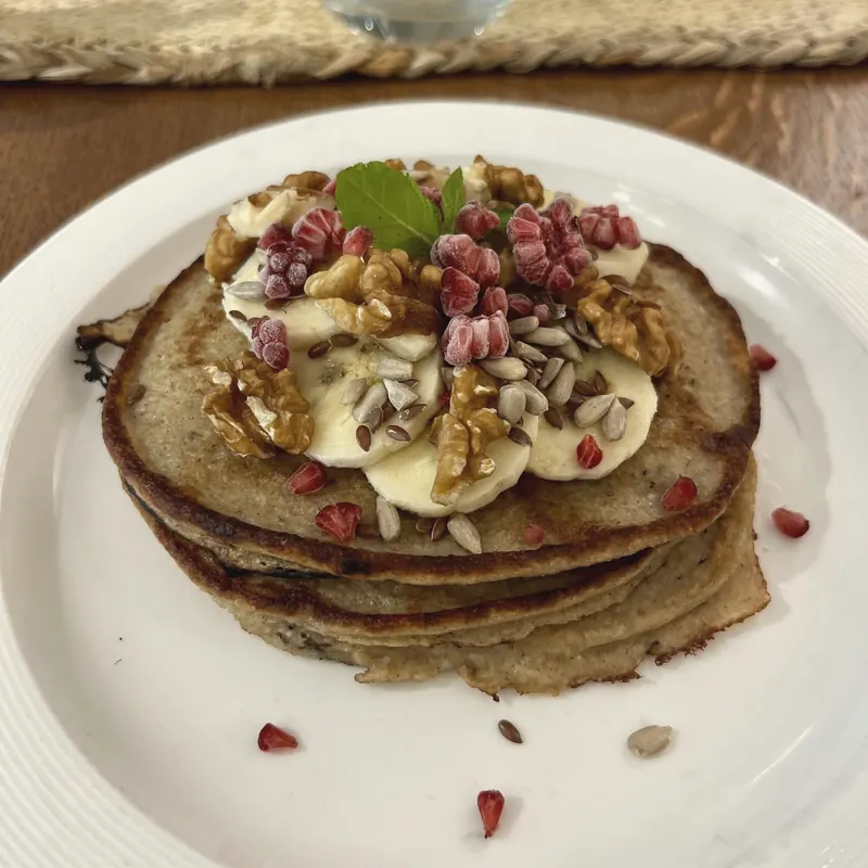 A stack of banana pancakes with walnuts, seeds and pomegranate