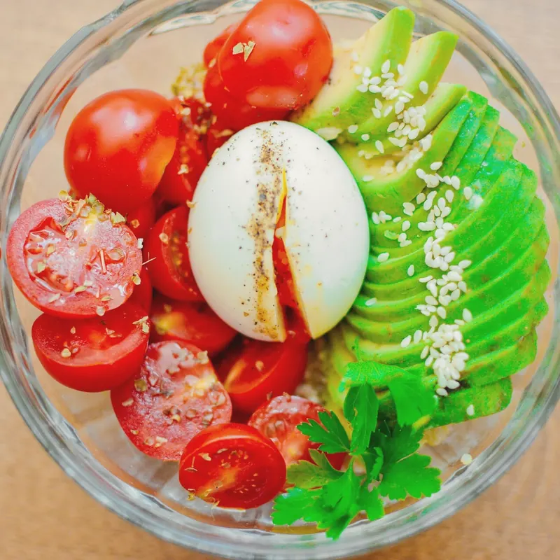 Glass bowl with cherry tomatoes, sliced avocado with sesame and a boiled egg
