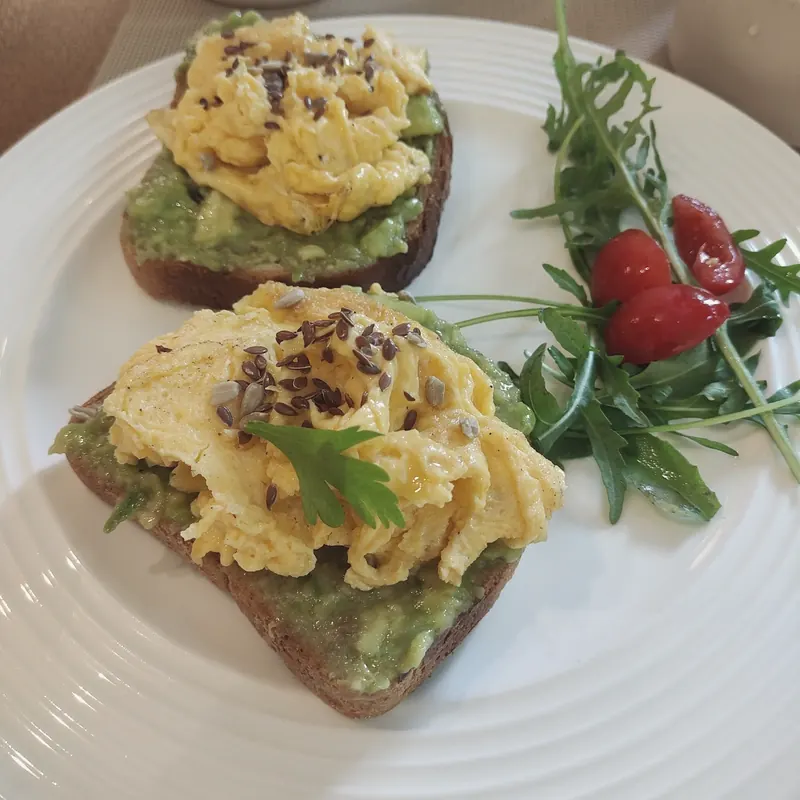 Two avocado toasts topped with soft scrambled eggs, with rocket and tomatoes