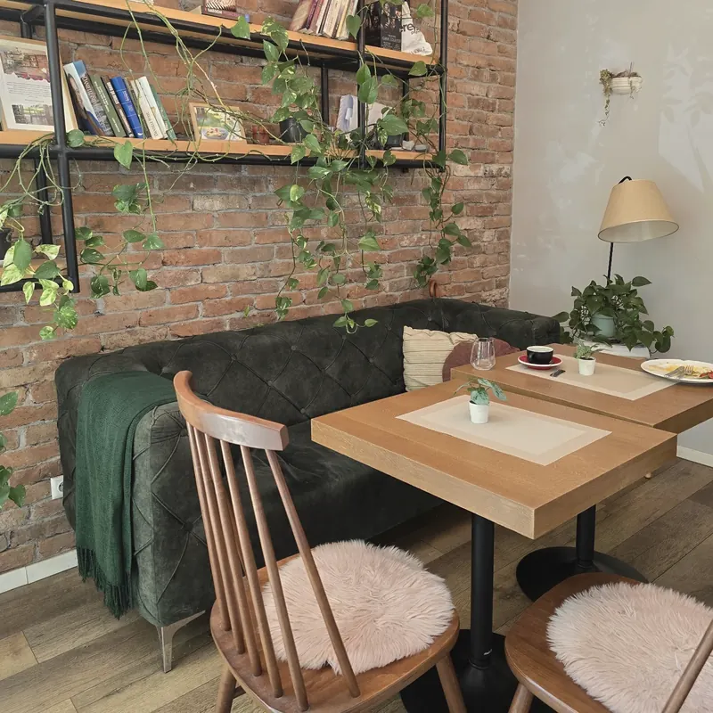 A corner of the café: green velvet sofa, brick wall with bookshelves and trailing plants, two small tables