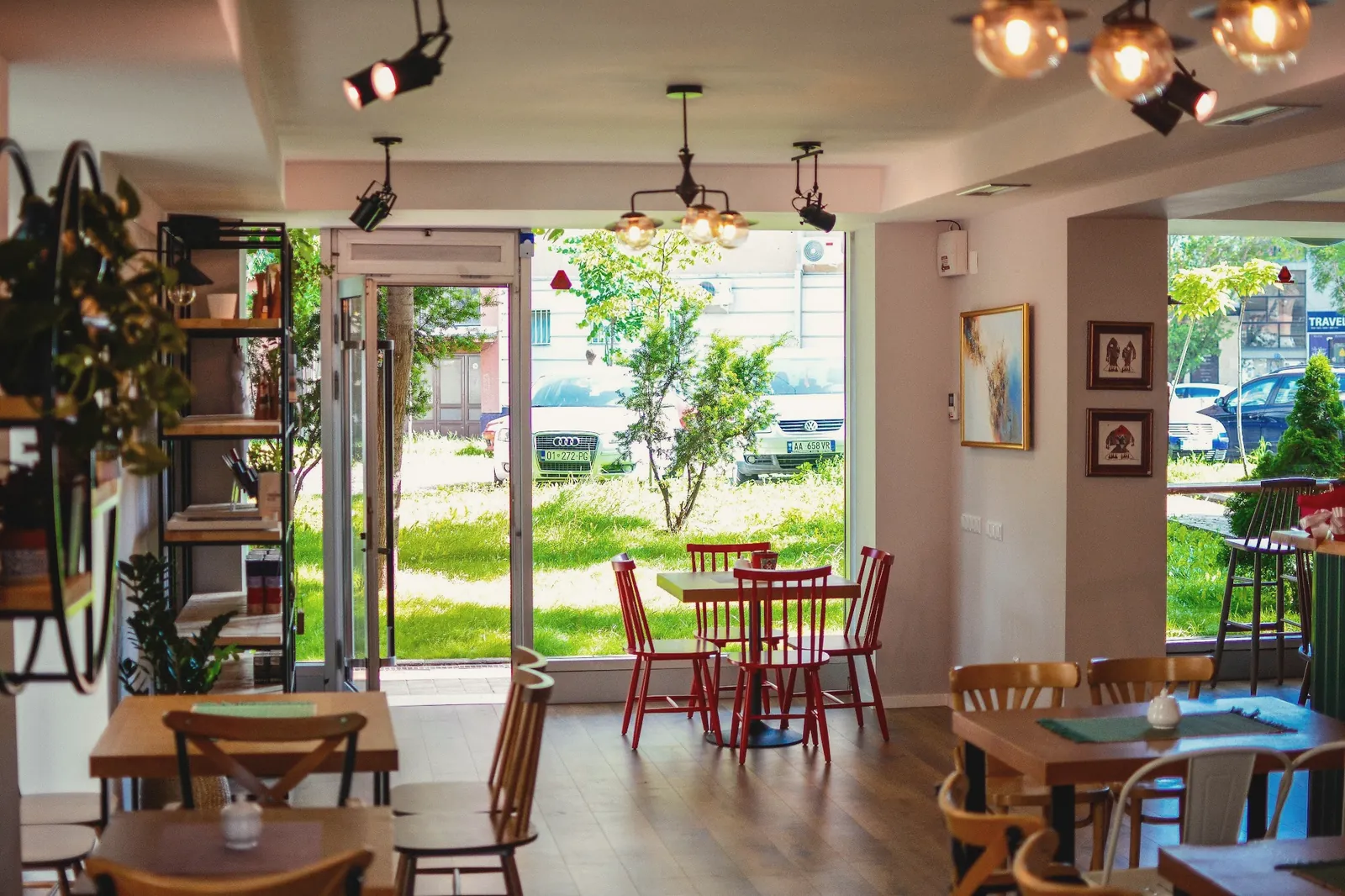 The bright dining room with wooden tables, red chairs and a garden view through the glass front
