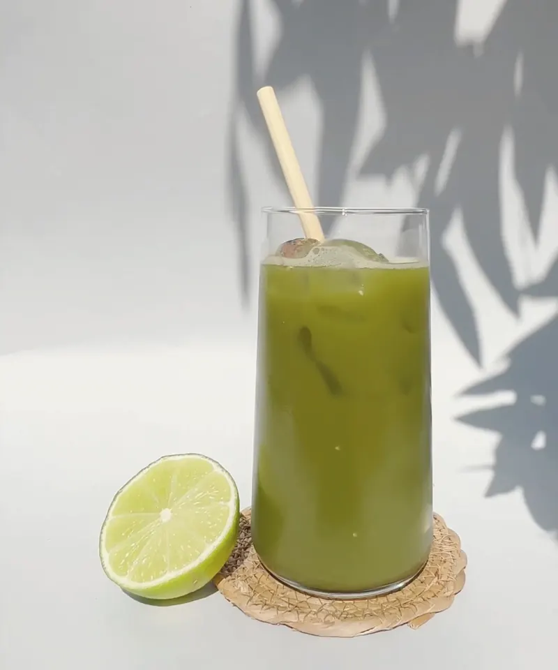 Iced matcha with a lime half on a cork coaster, leaf shadows on the wall