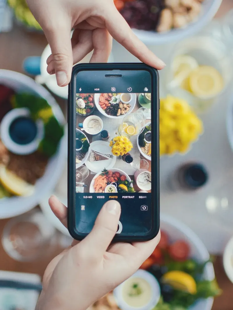 Hands taking a phone photo of a table full of brunch plates