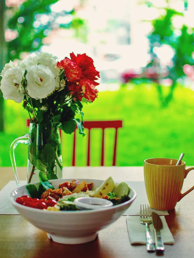 Flowers in a glass jug, a salad bowl and a yellow mug on a table by the garden window